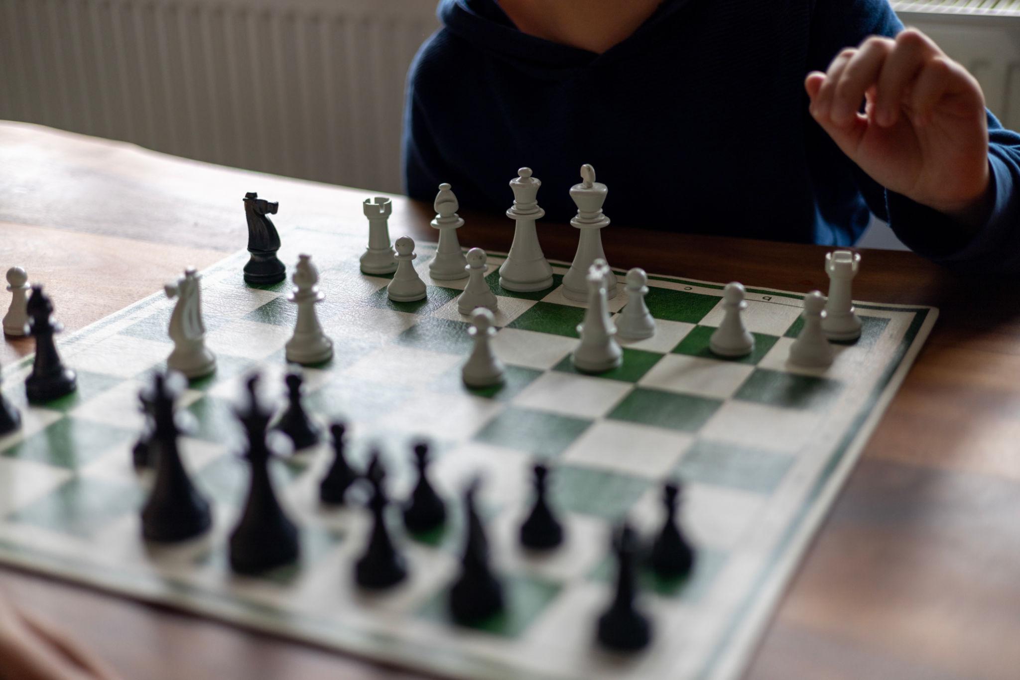 A child at home, focused on the next move over a chessboard.