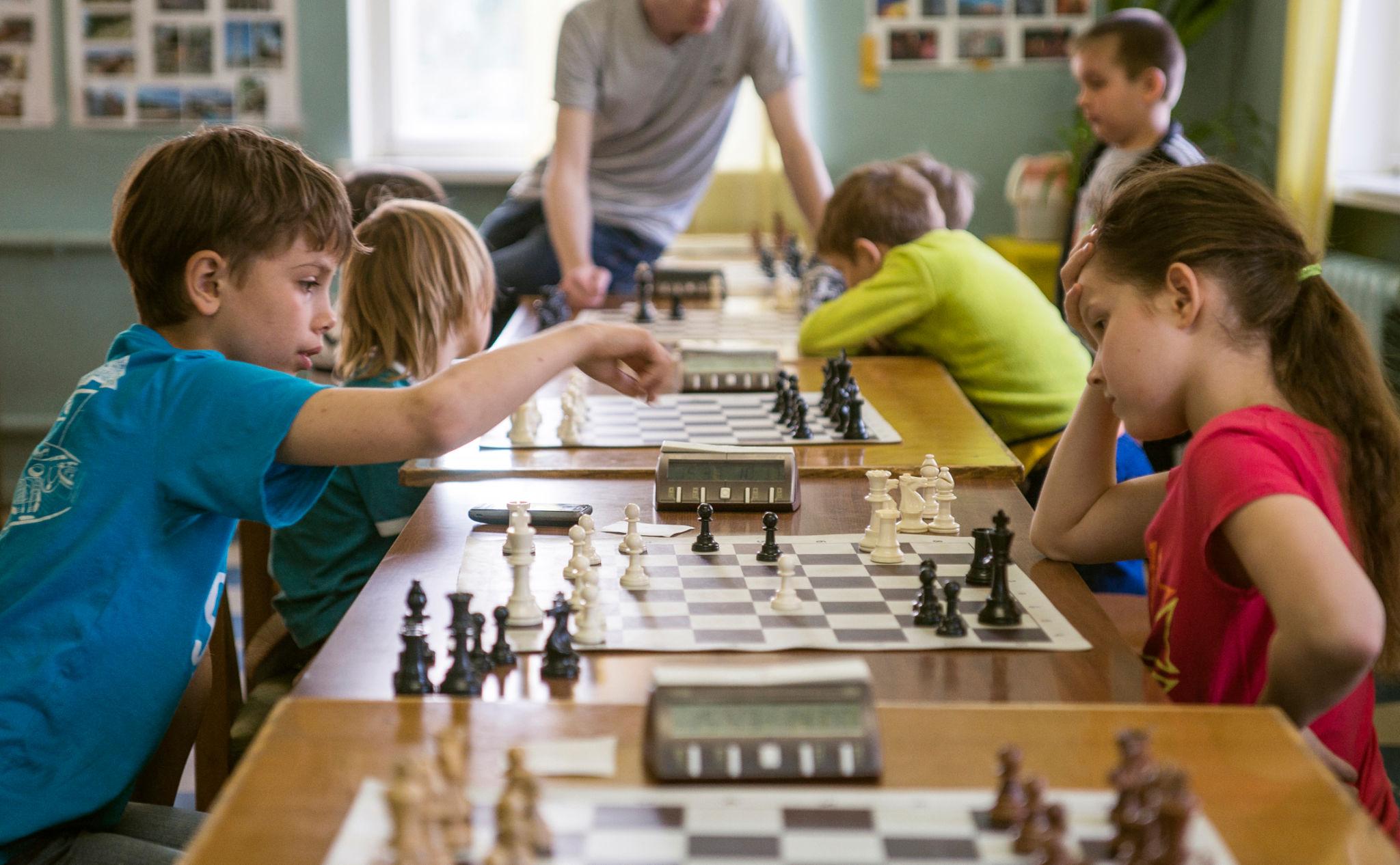 Children at a chess club, playing across long tables with clocks.