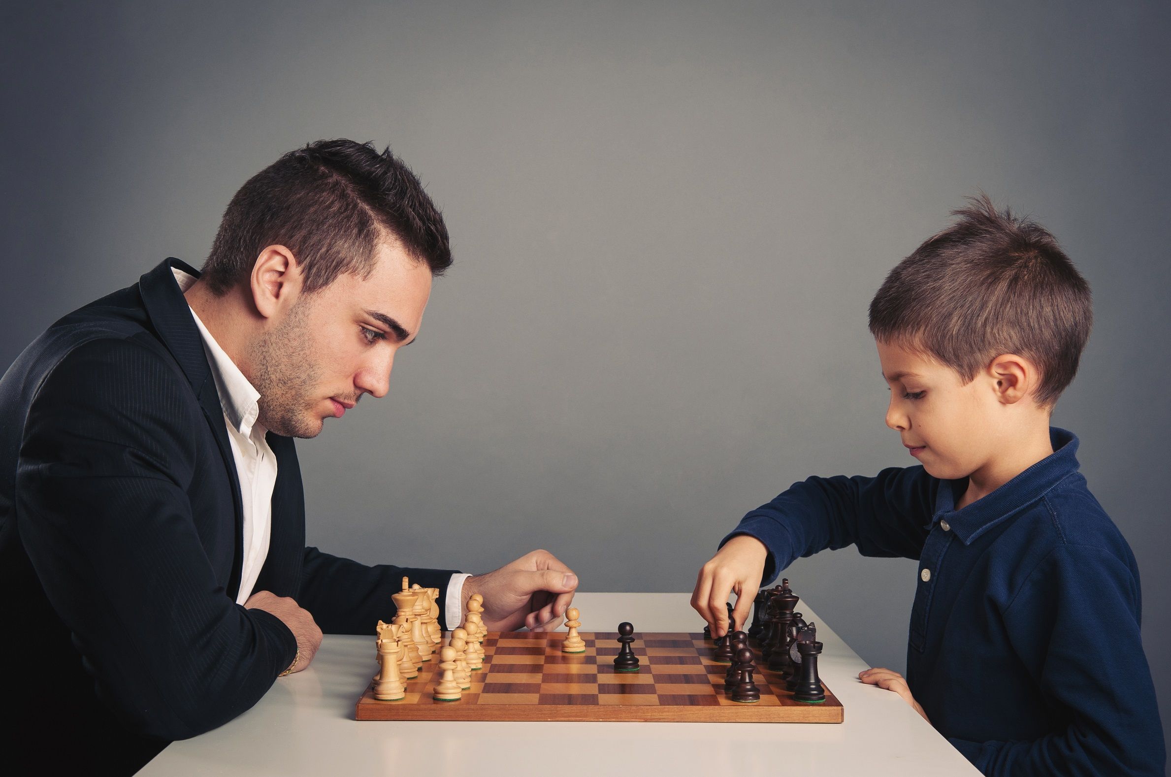 A parent and child sitting across a chessboard, mid-game.